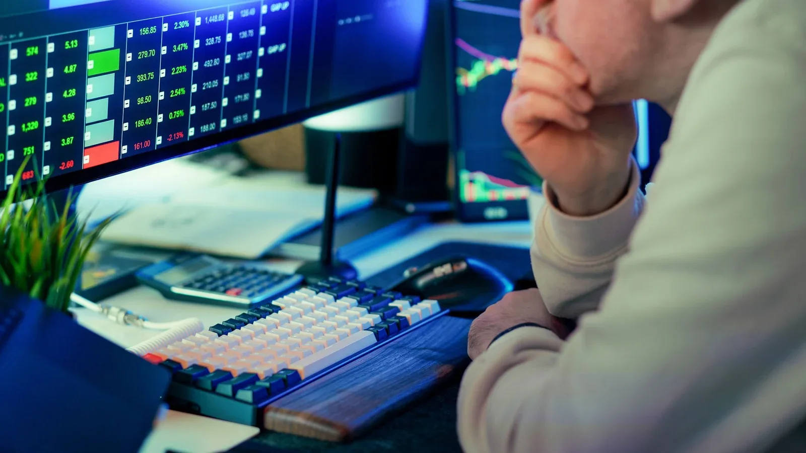 Trader studies market charts on multiple computer screens in a modern office.