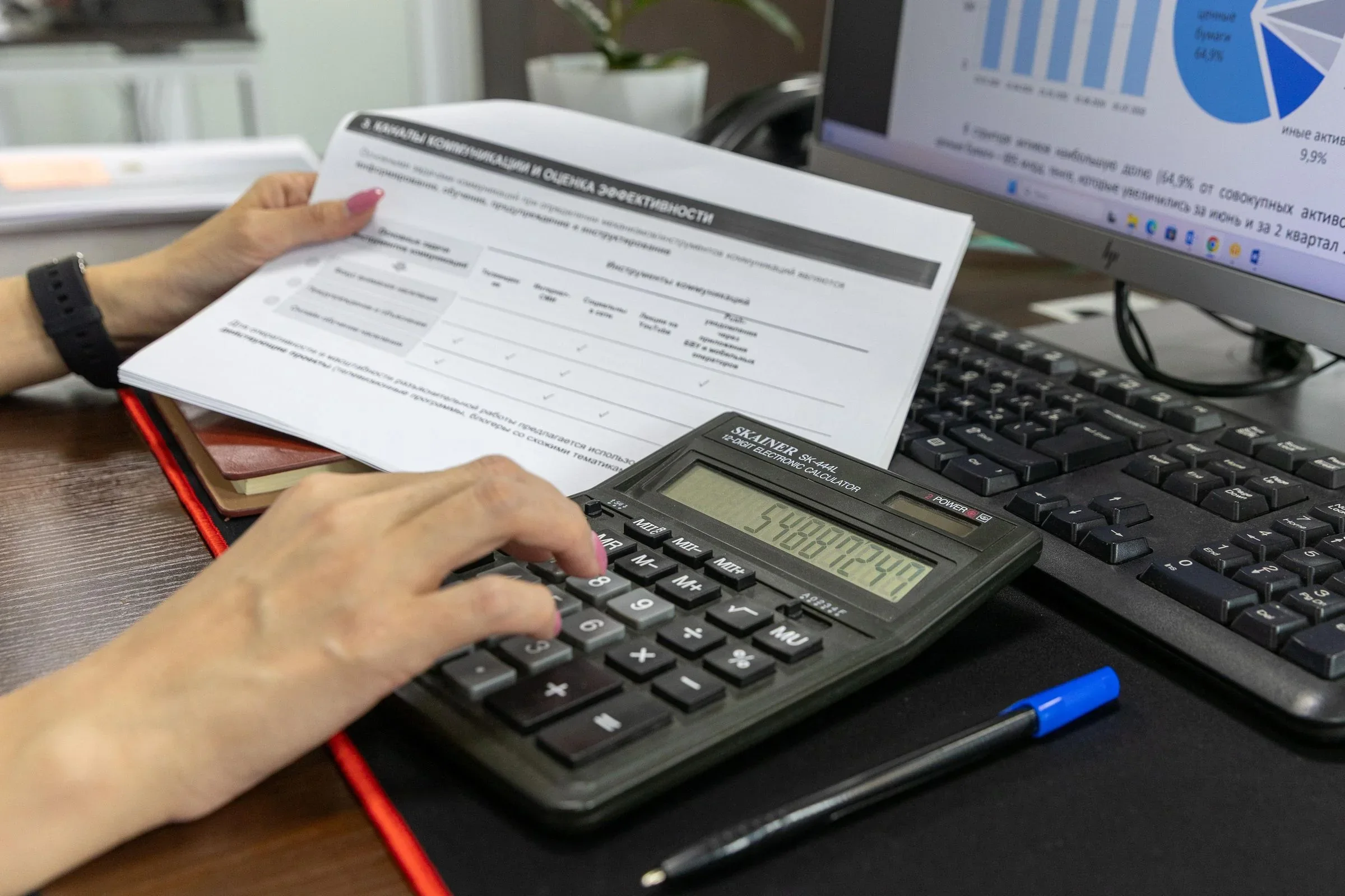 A person using a calculator while reviewing a printed financial report at an office desk.