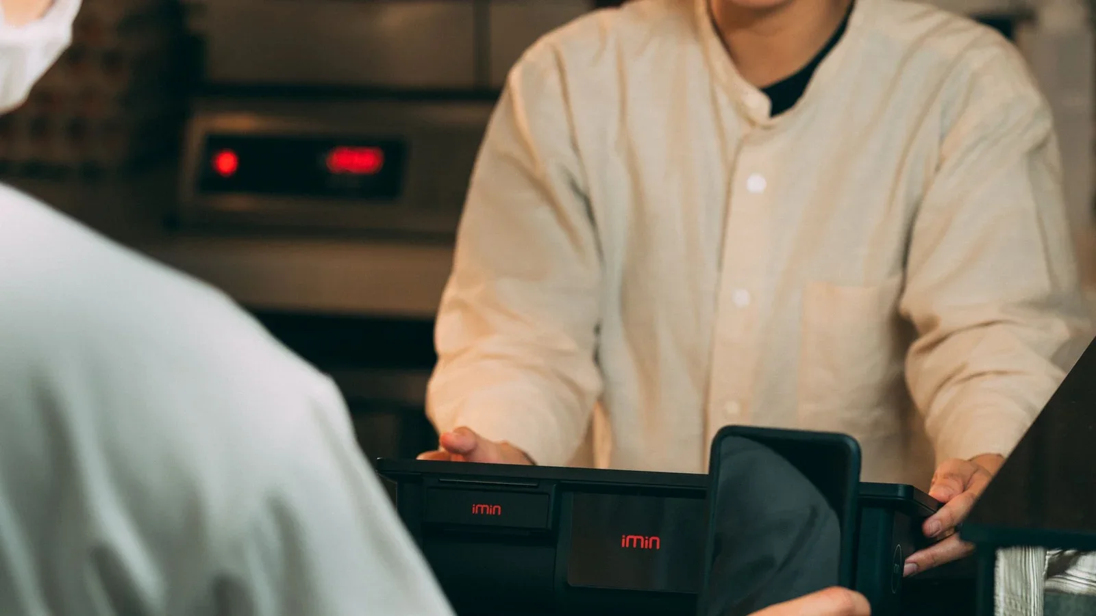 Customer holds a smartphone near a payment terminal during a digital payment.